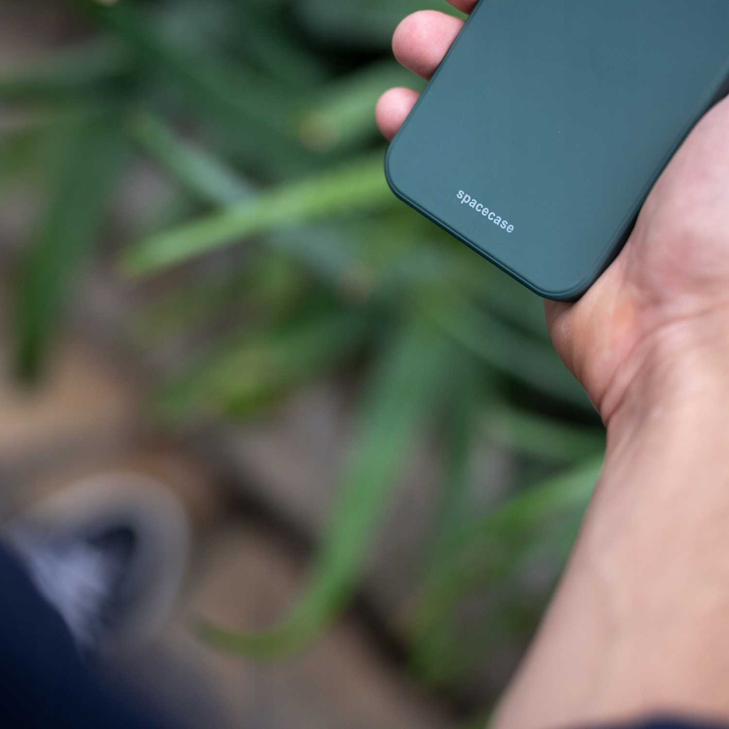Ręka trzymająca zielone etui na telefon z logo Spacecase z zielenią w tle.