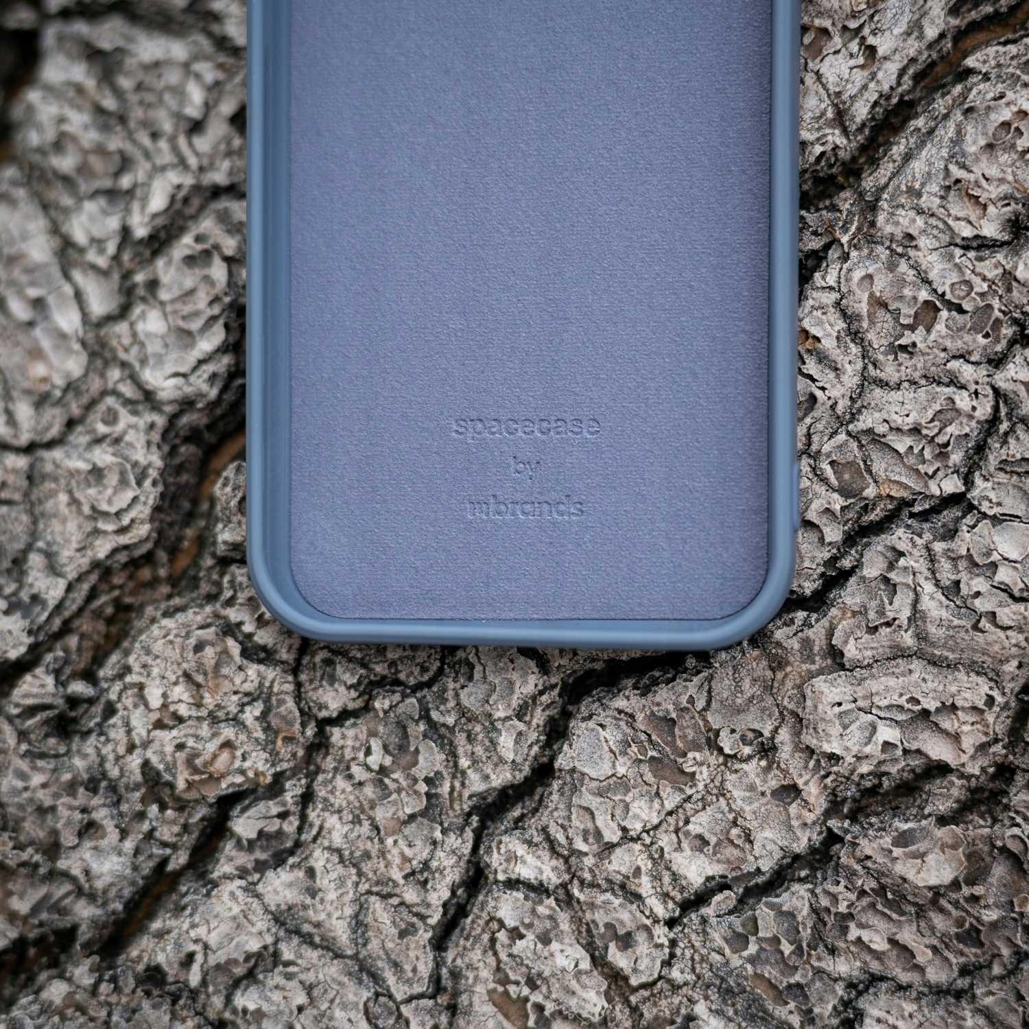 Niebieskie etui na telefon leżące na korze drzewa, widoczna nazwa marki.