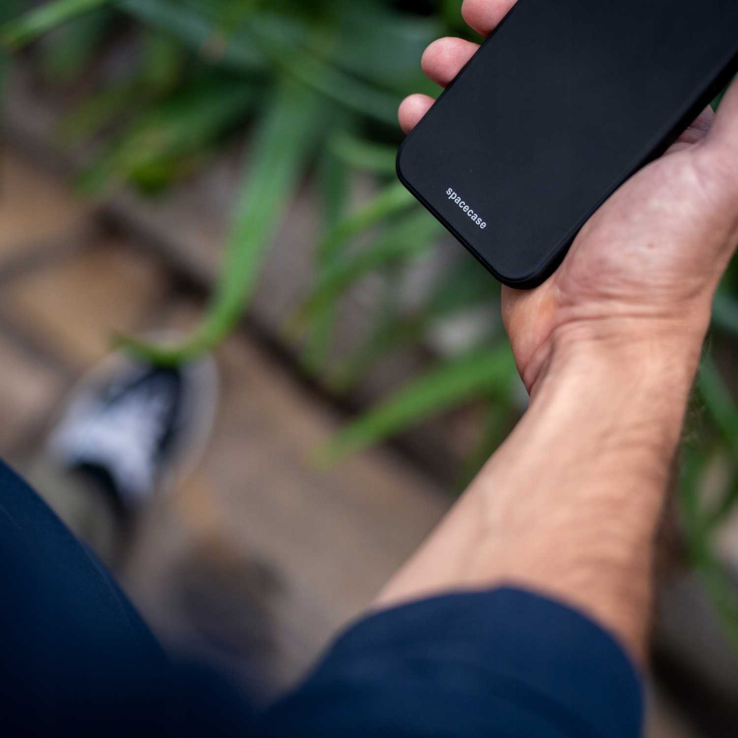 Ręka trzymająca czarne etui na telefon z napisem 'spacecase'. Tło jest rozmyte.