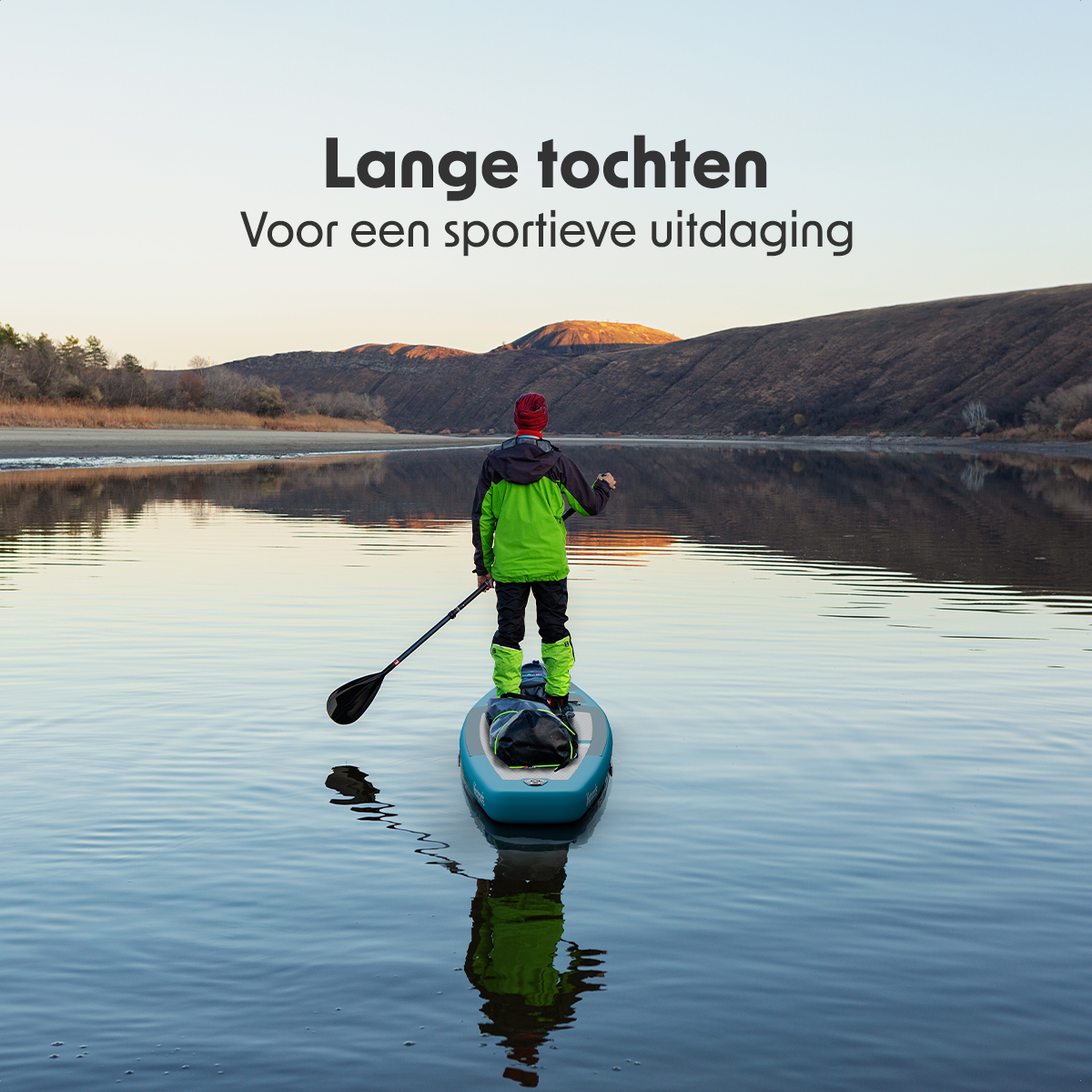 Persoon peddelt op een blauw board in kalm water, met heuvels op de achtergrond.