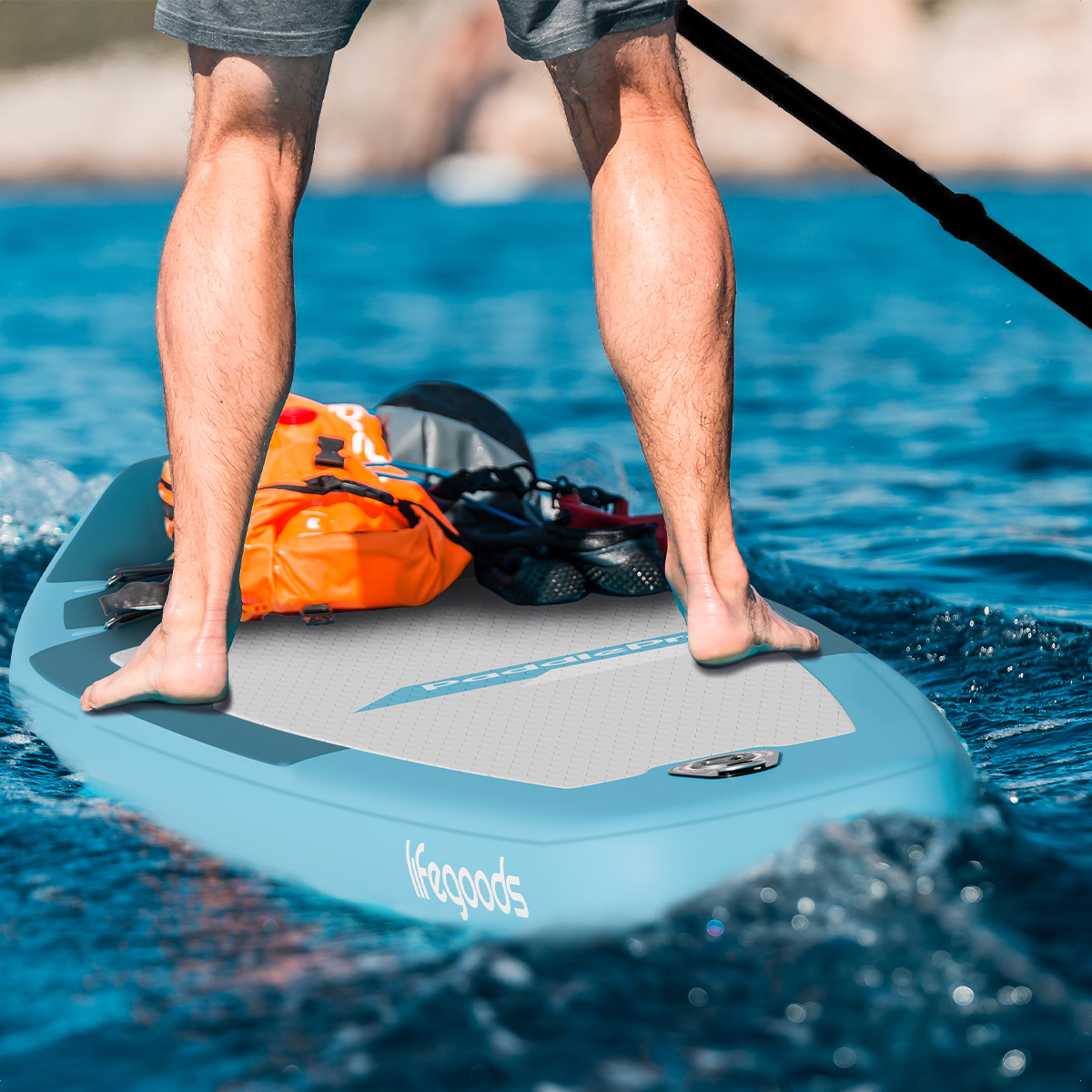 Een persoon staat met uitrusting op een blauwe paddleboard op blauw water.