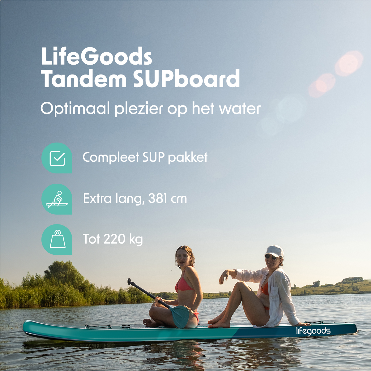Zwei Frauen sitzen auf einem blauen Paddleboard im Wasser mit Bäumen im Hintergrund unter einem hellen Himmel.