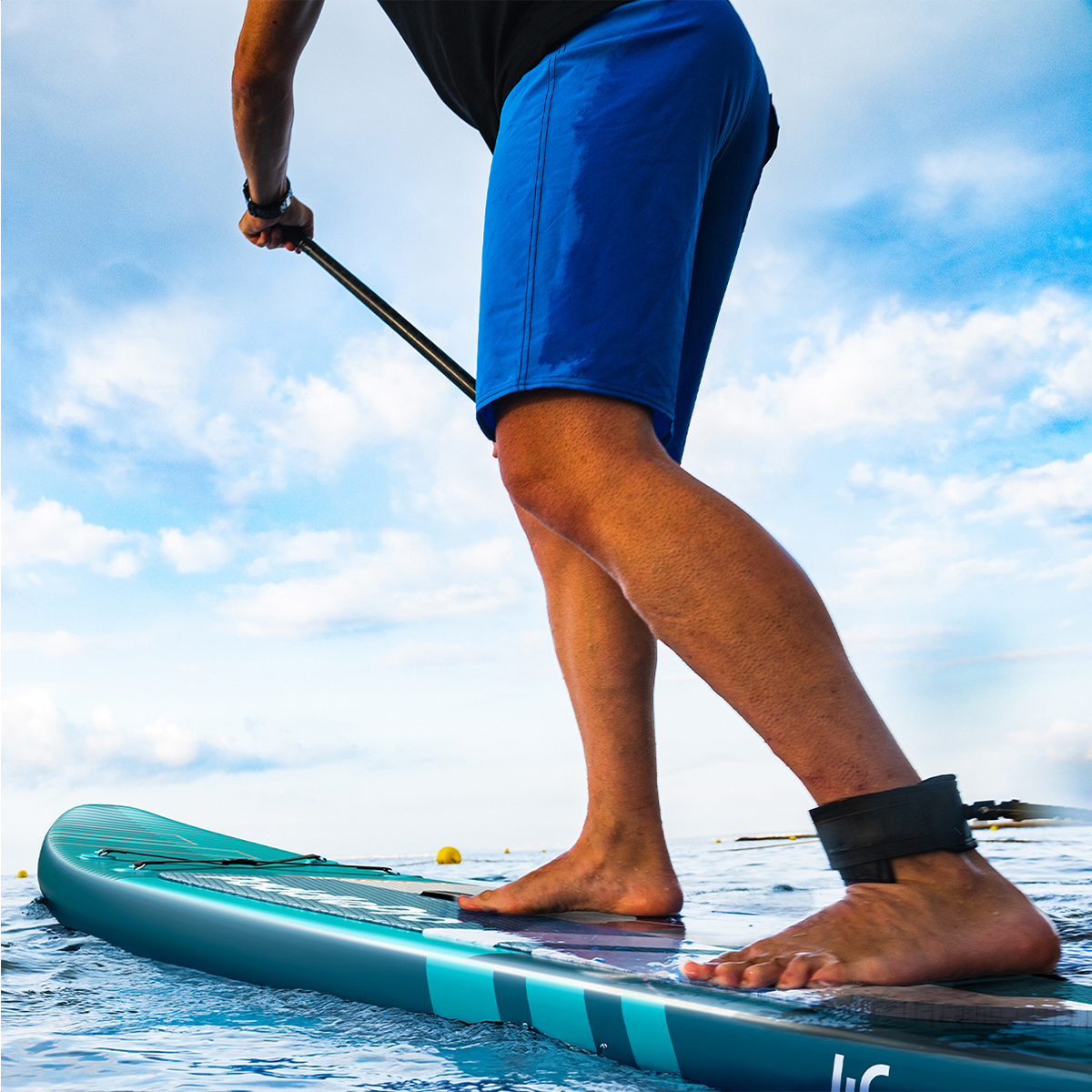 Een persoon peddelt op een blauw paddleboard in de oceaan onder een bewolkte lucht.