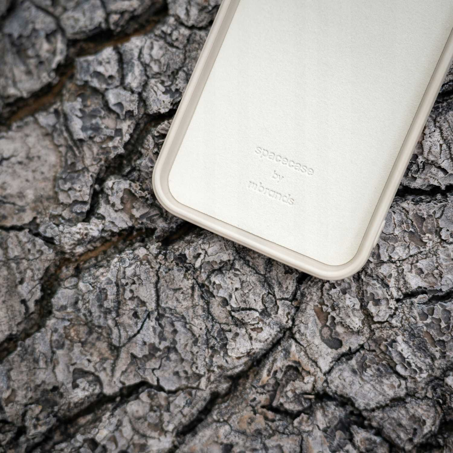 Kremowe etui na telefon z logo „spacecase” na tle kory drzewa.