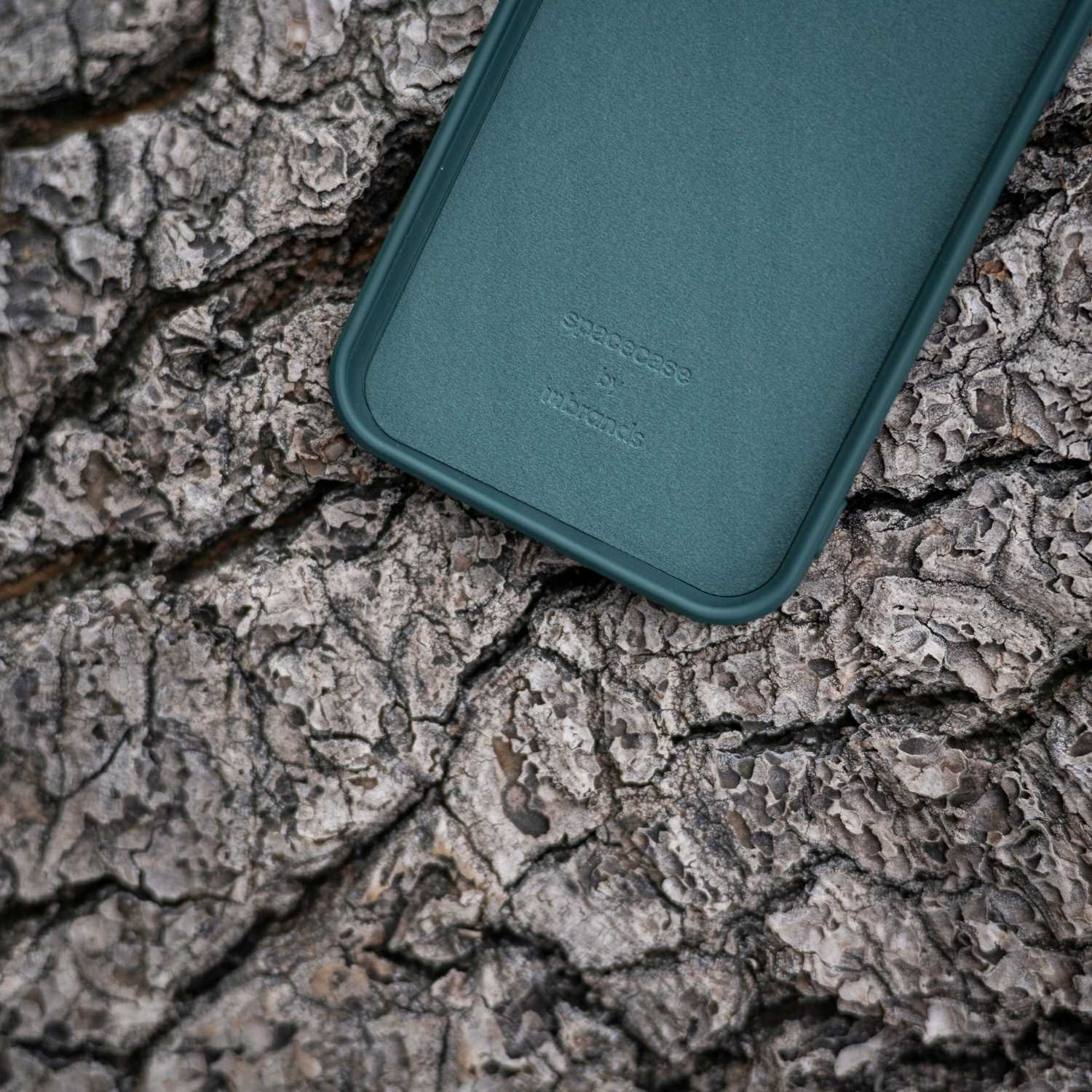 Ciemnozielone etui na telefon 'spacecase' na tle szorstkiej, teksturowanej kory drzewa.