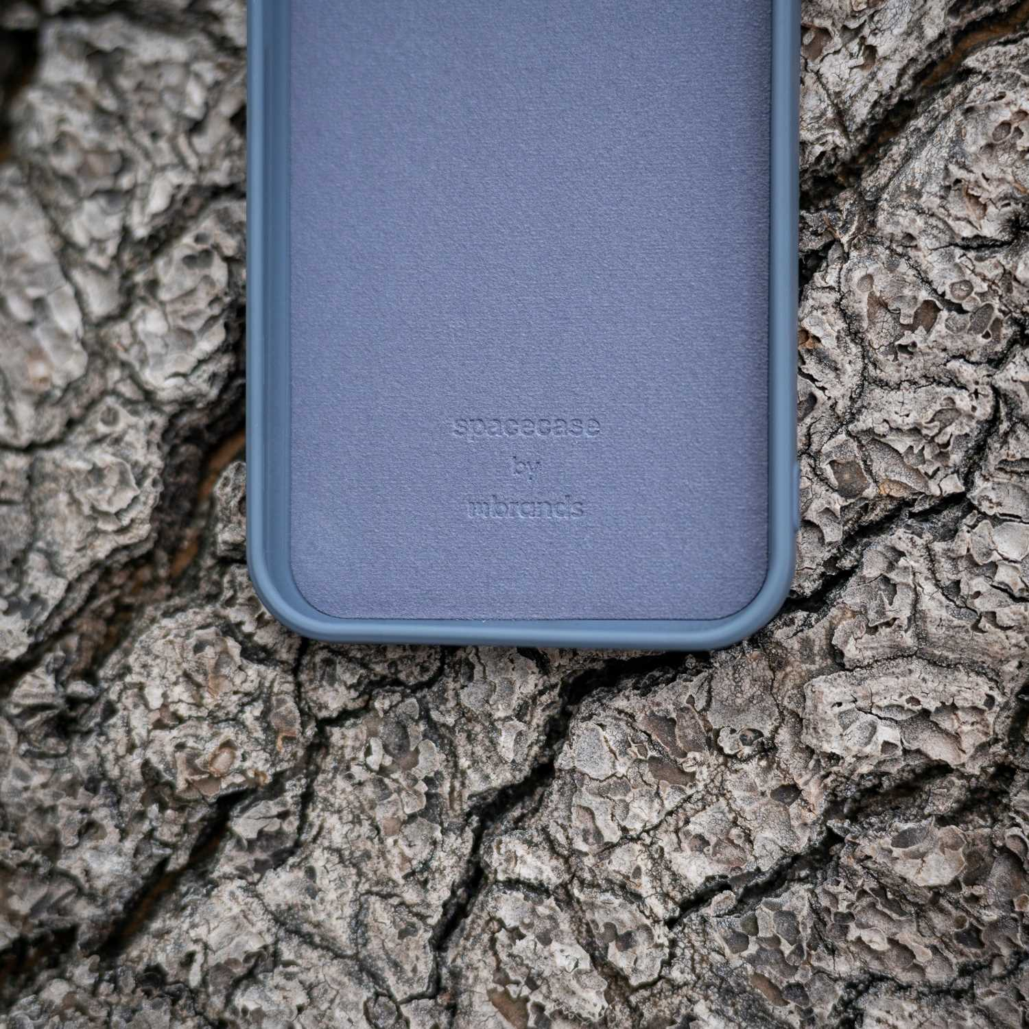 Zbliżenie niebieskiego etui na szorstkiej korze. Etui z nadrukiem 'spacecase by mbrands'.