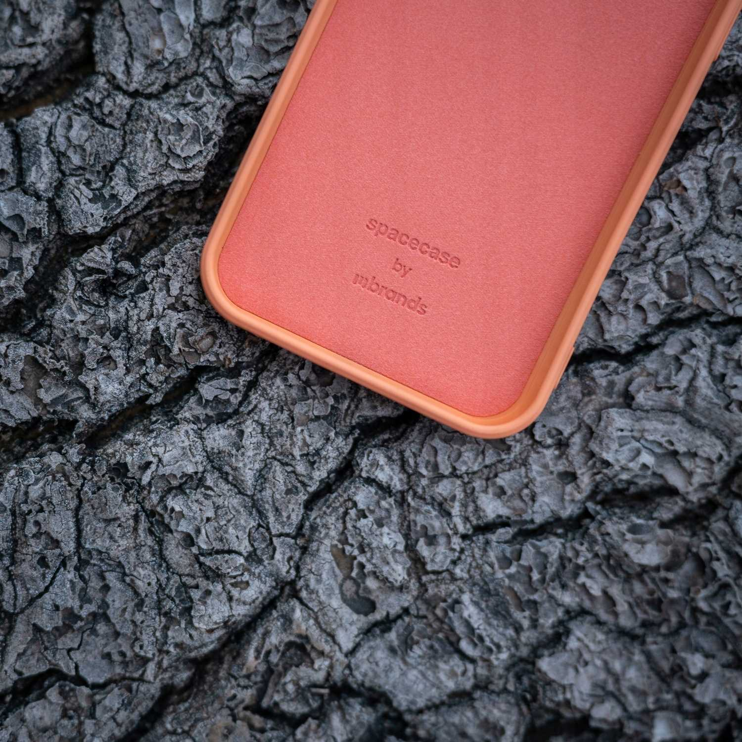 Zbliżenie pomarańczowego etui na telefon z logo „spacecase by mbrands” na teksturowanej szarej powierzchni.