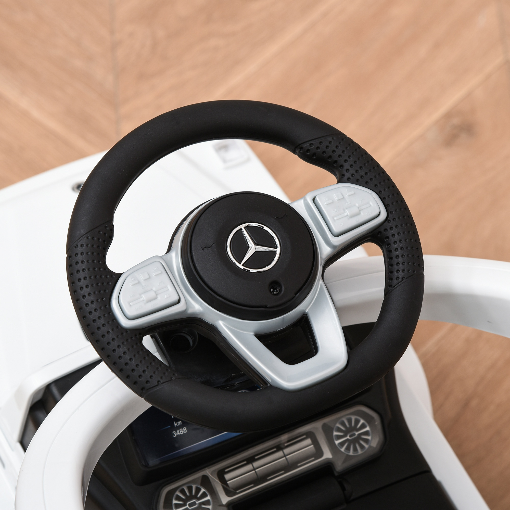 Primer plano del volante de un coche de juguete blanco con el logo de Mercedes. Cuero negro y detalles plateados.