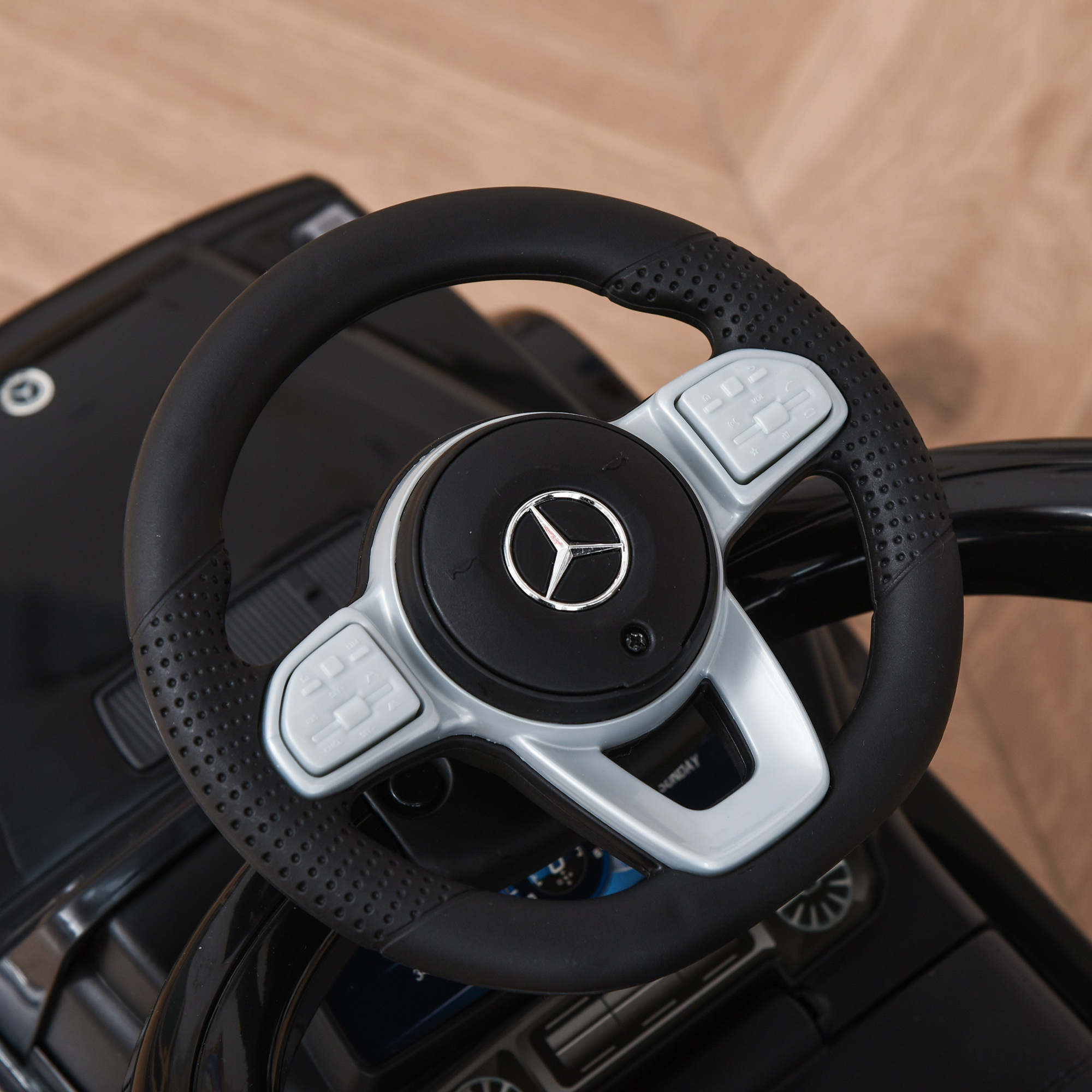 Primer plano del volante de un coche de juguete negro con el logo de Mercedes. Cuero negro y detalles plateados.