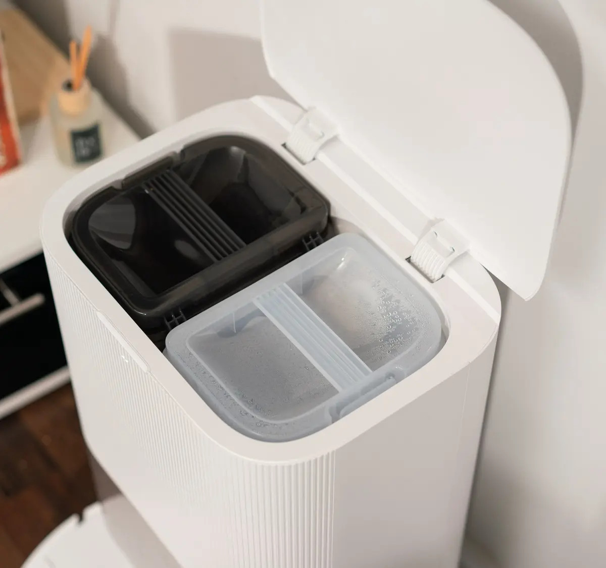 Biały robot odkurzający z otwartą pokrywą, która odsłania dwa pojemniki.