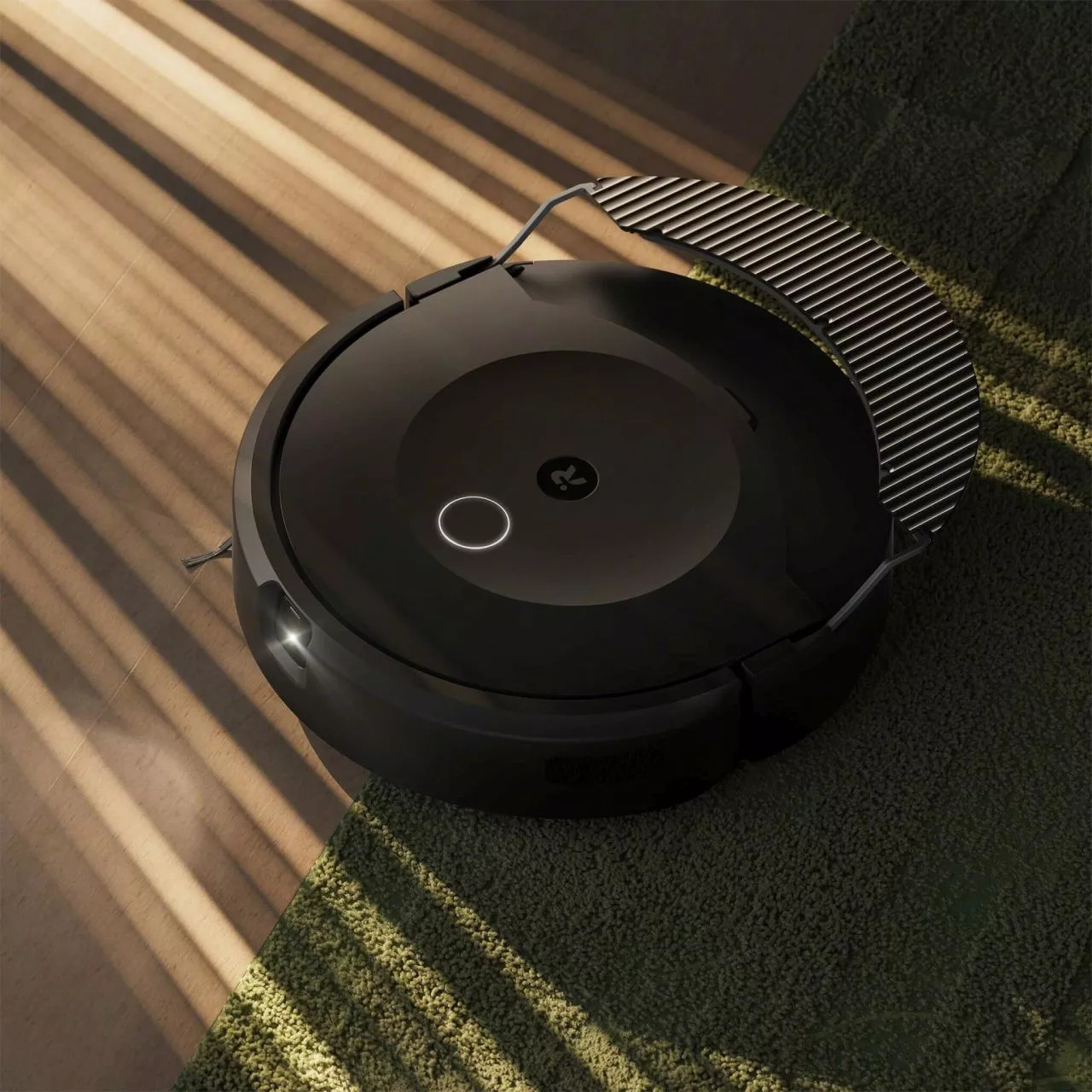 Czarny robot odkurzający Roomba jest pokazany na zielonym dywanie, co podkreśla jego elegancki wygląd.