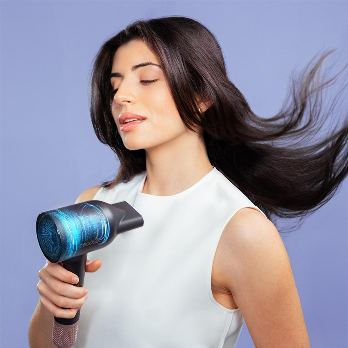 Een vrouw houdt een zwarte haardroger vast en kijkt naar rechts. De droger heeft een blauw display.
