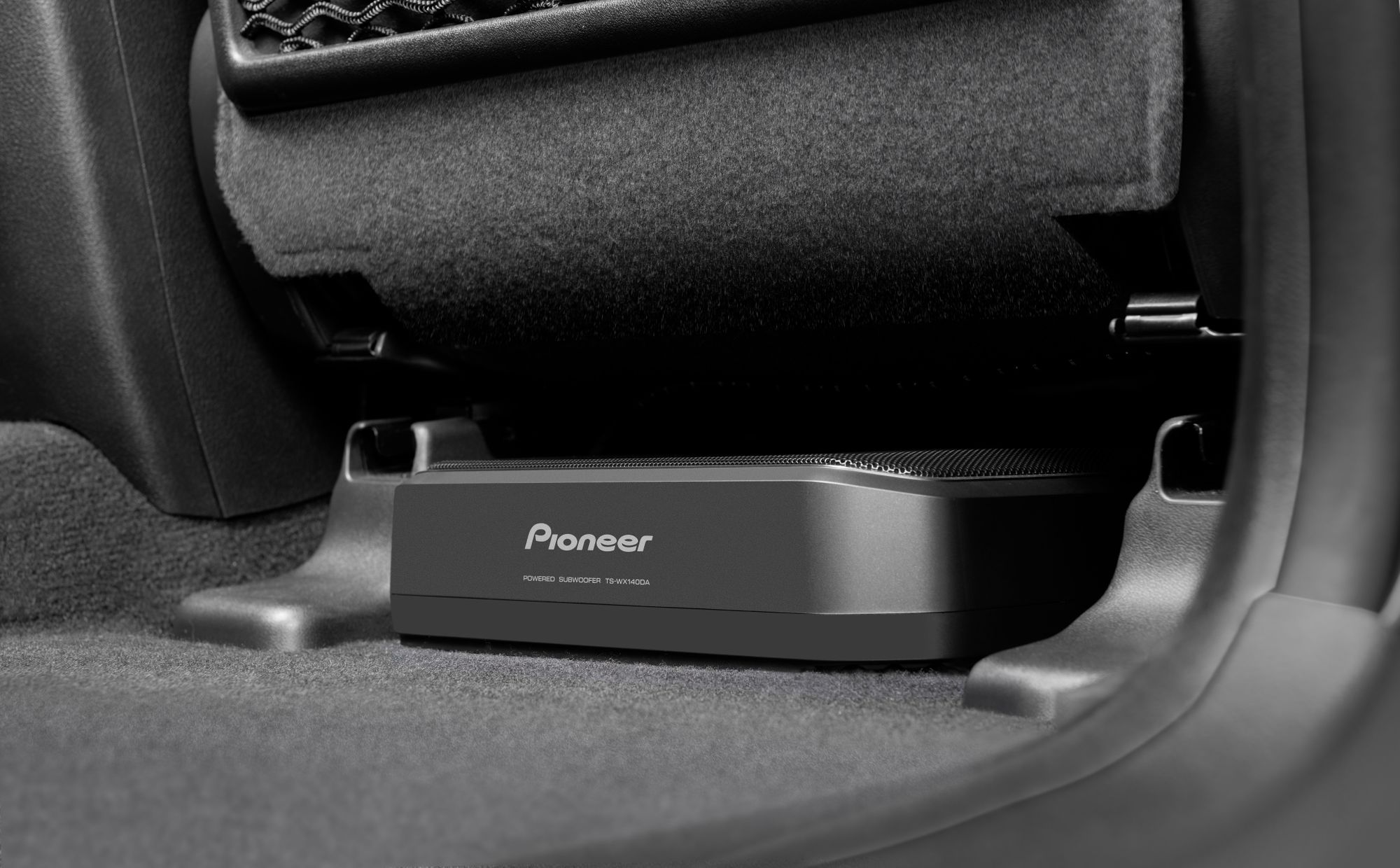 Un subwoofer Pioneer nero posizionato sotto il sedile di un'auto sul pavimento.