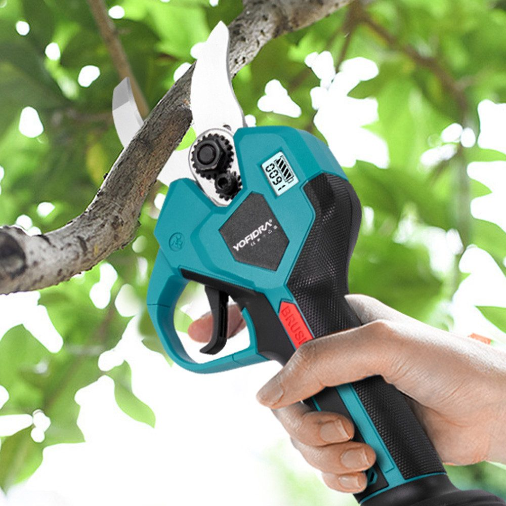 Una mano sostiene podadoras eléctricas verde azulado cortando una rama, con hojas verdes de fondo.