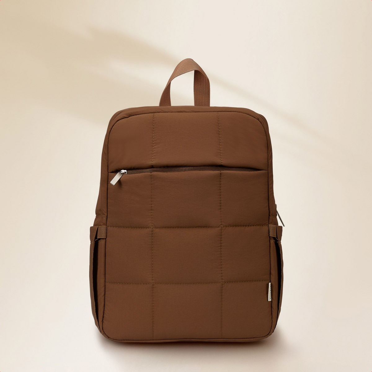 Brown quilted backpack with a top handle, front zipper, and side pockets. Studio shot.