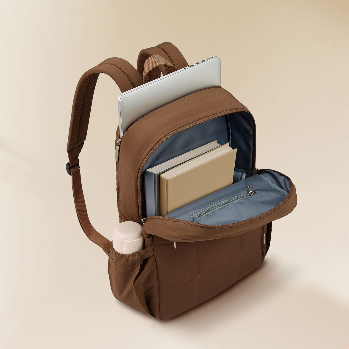 Brown quilted backpack with laptop and books inside, side water bottle pocket visible.