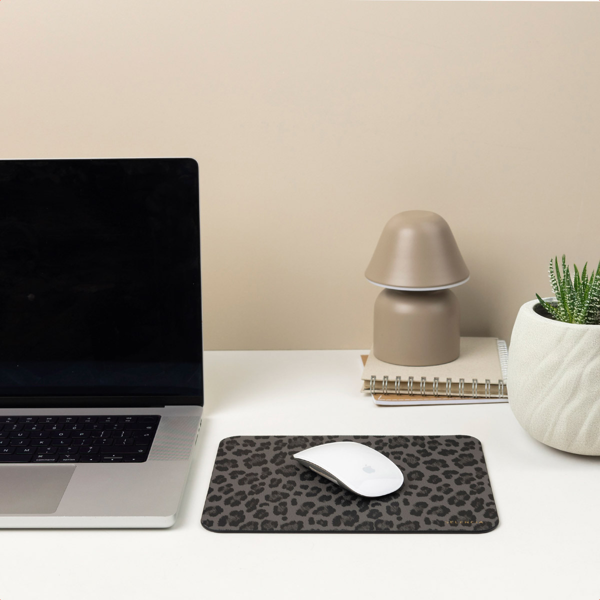 A desk setup featuring a laptop, mouse, lamp, and plant on a leopard print mousepad.