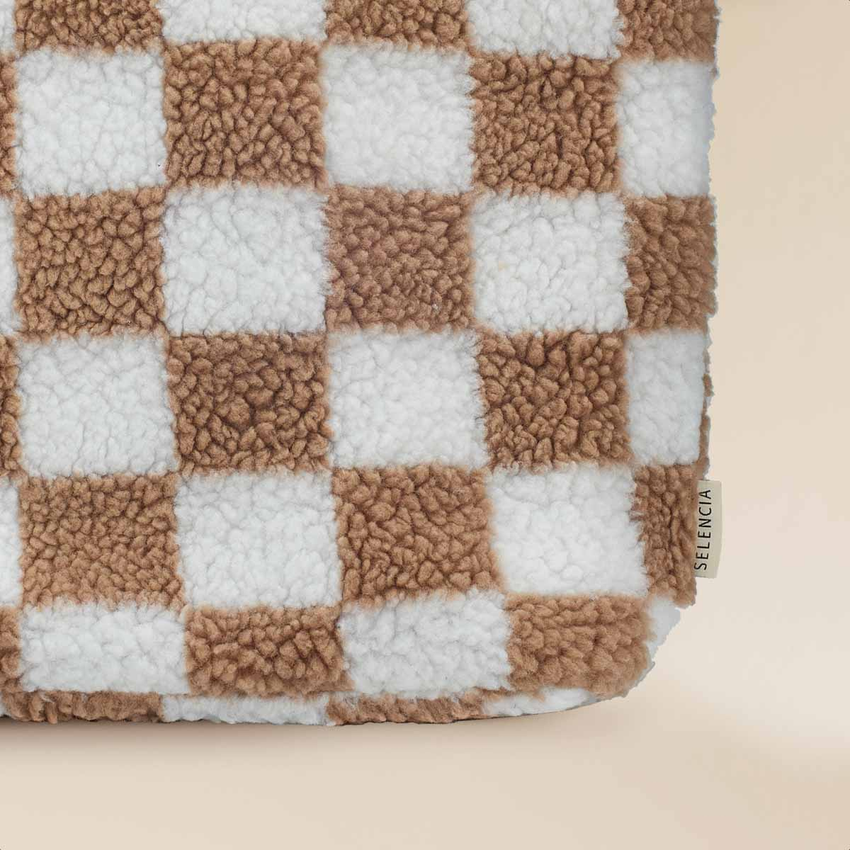Close-up of a checkered bag with alternating white and brown squares on a beige background.