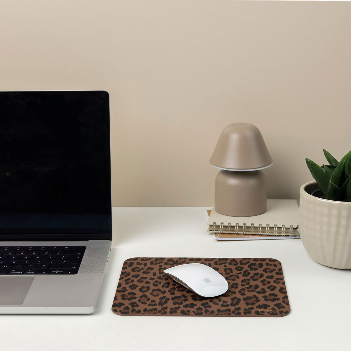 A desk setup featuring a laptop, lamp, mousepad with leopard print, and a white mouse.