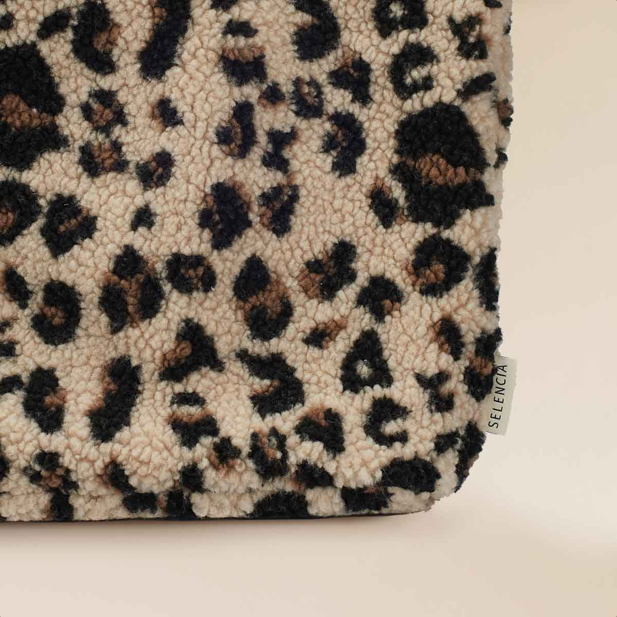 A close-up of a sherpa tote bag with brown, cream, and black leopard print.