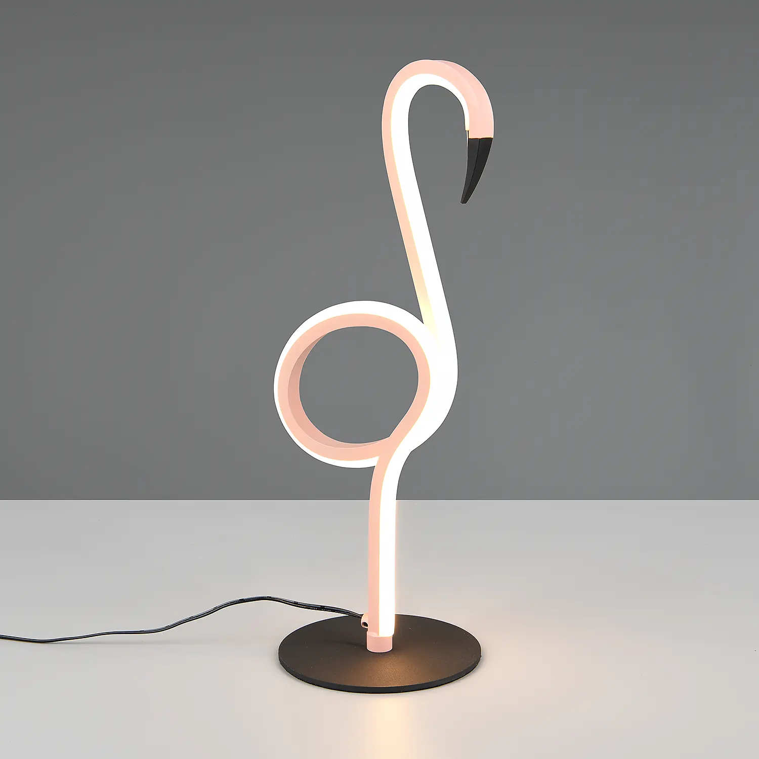 Flamingolamp met een roze nek en wit lichaam, staande op een zwarte voet op een witte tafel.