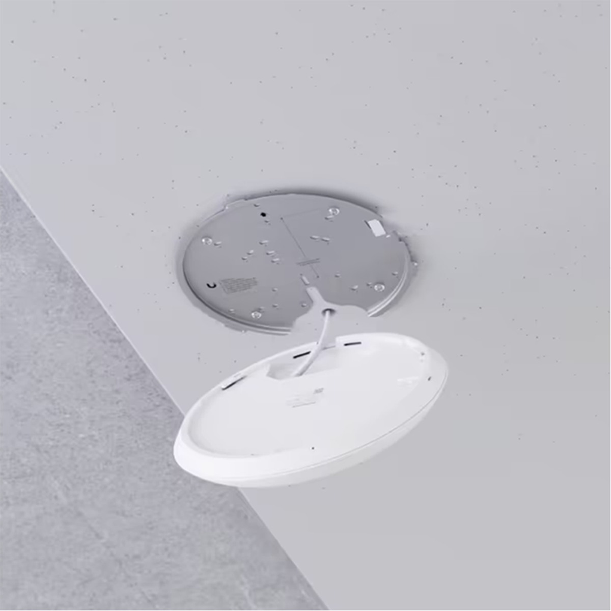 A white round device is being installed on a gray ceiling with a cable hanging.