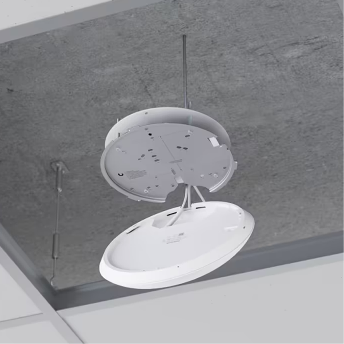 A white round device is being installed on a gray ceiling with a metal rod holding it.