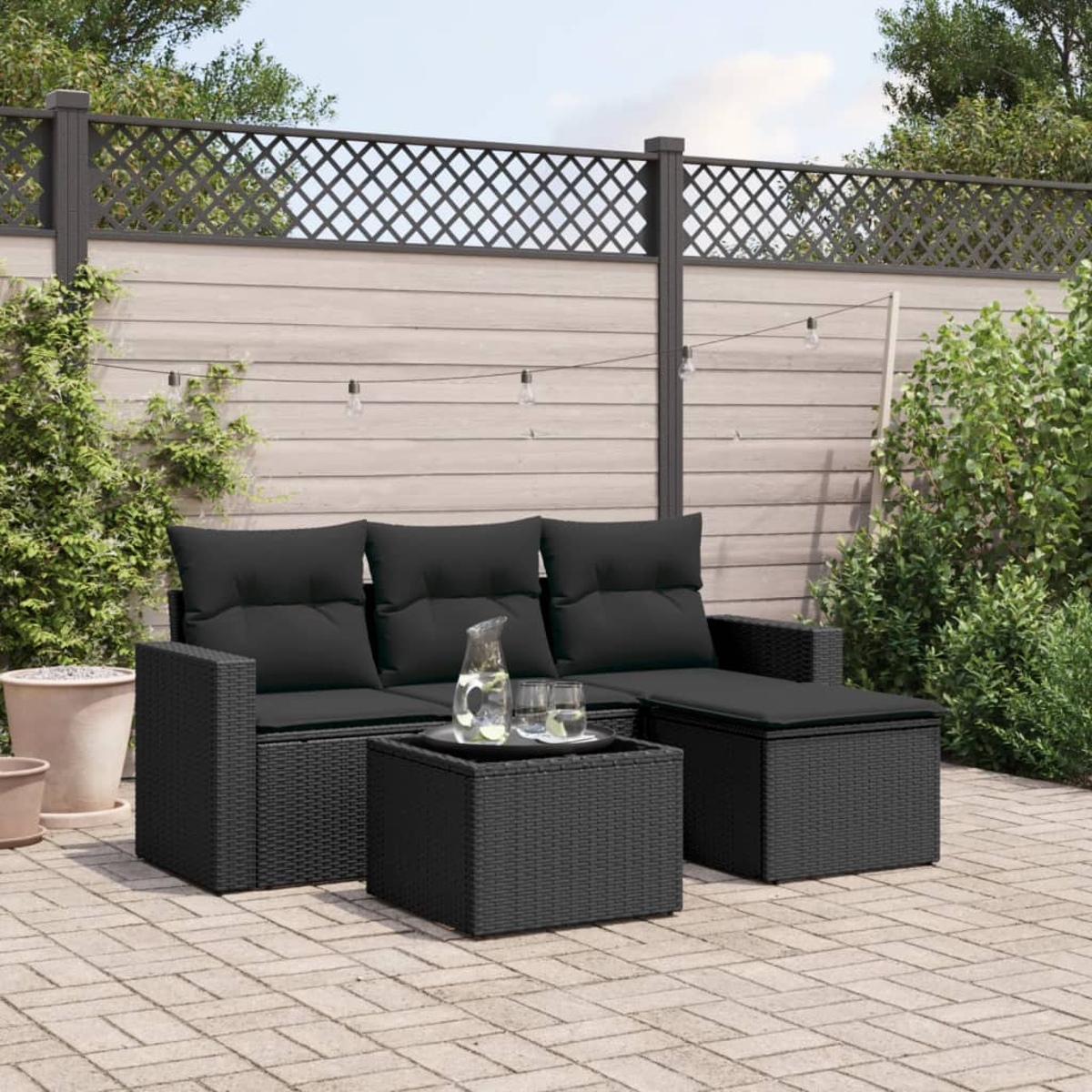Ein schwarzes Outdoor-Sofaset mit Kissen, einem Tisch und einem dekorativen Zaun.
