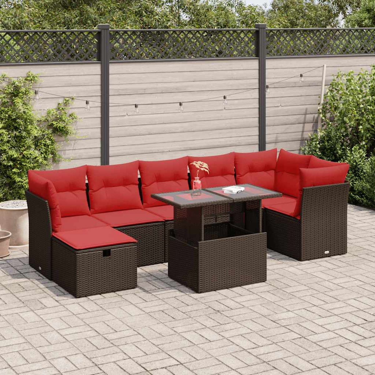 Gartenmöbel mit braunen Rattanmöbeln und roten Kissen auf einer Backsteinterrasse mit Lichterketten.