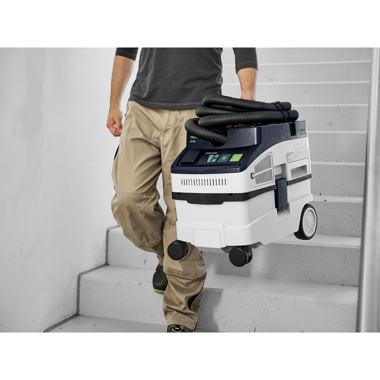 Un uomo che trasporta un aspirapolvere Festool giù per una rampa di scale.