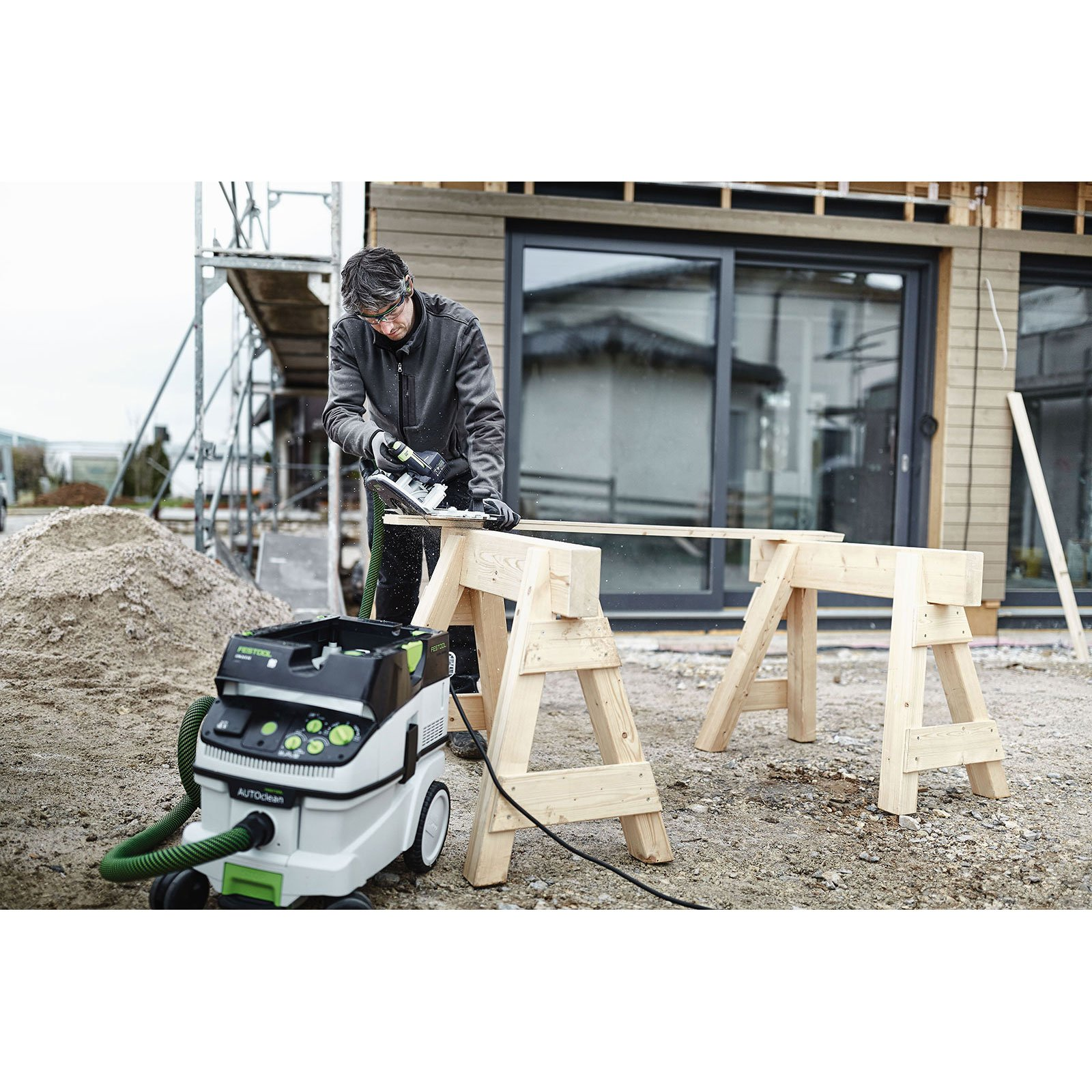 Mann sägt auf Holzbrettern, mit einem Festool Staubsauger in der Nähe auf einer Baustelle.