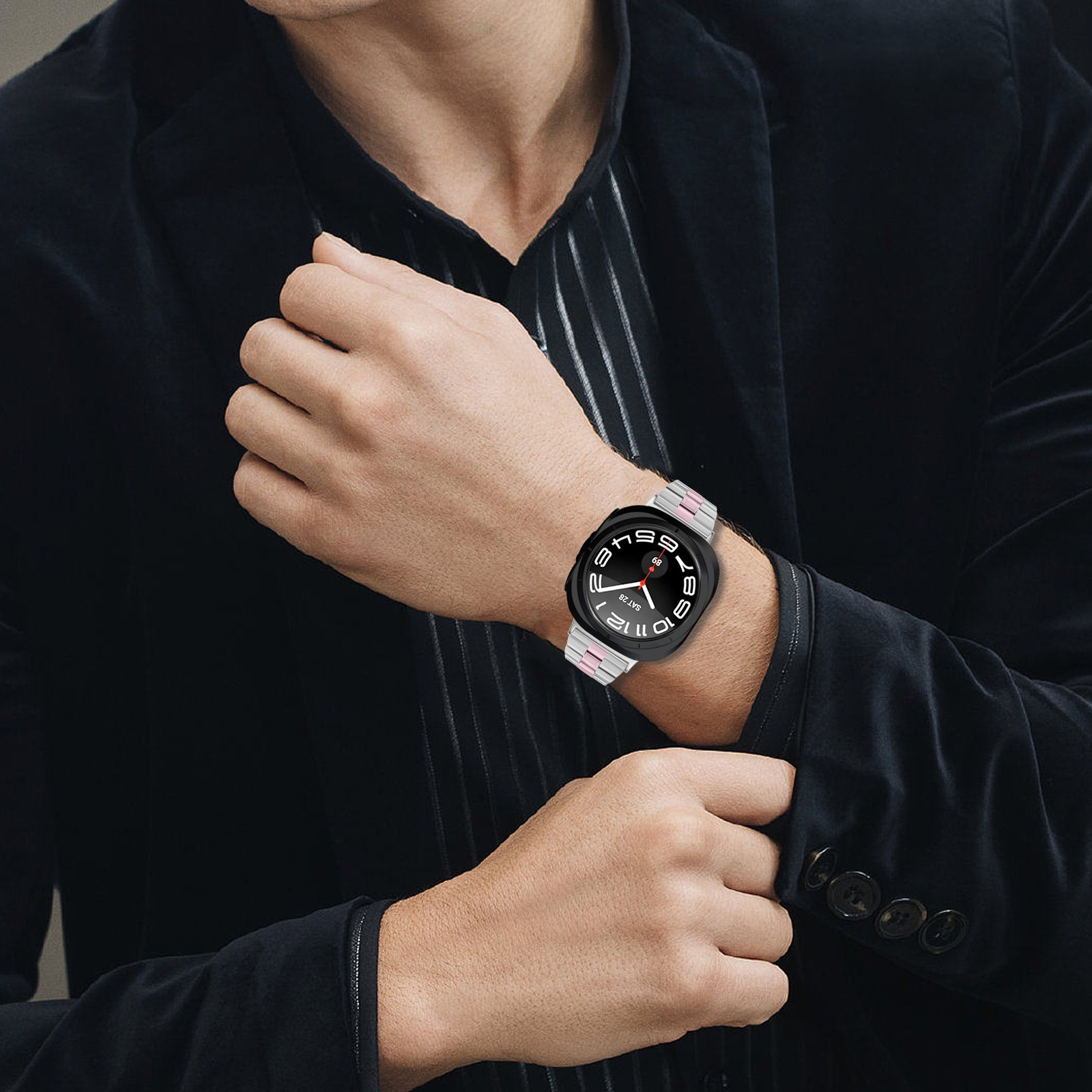 Mann im Anzug, der eine Smartwatch mit einem silbernen und rosafarbenen Metallarmband an seinem Handgelenk präsentiert.