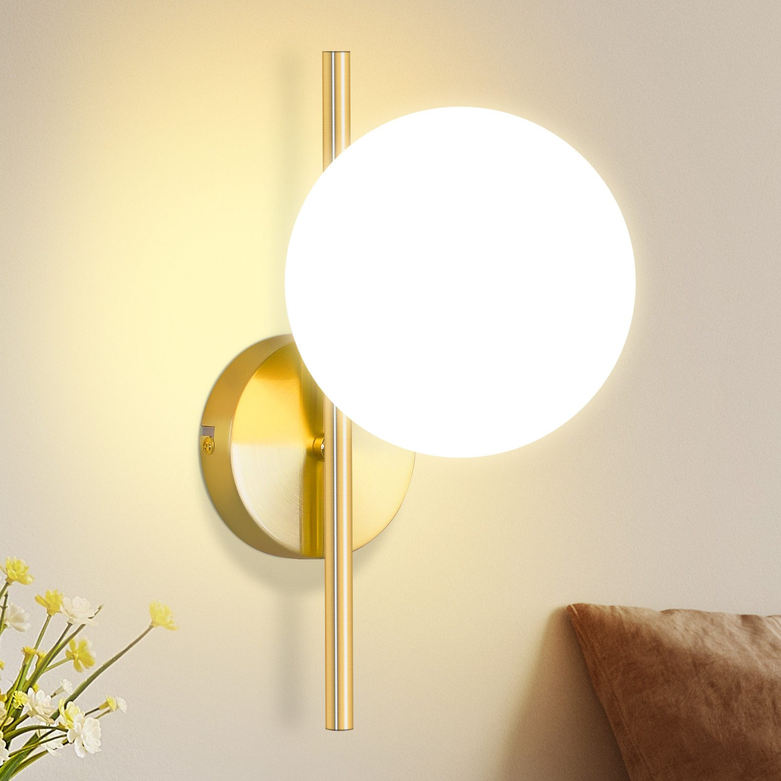 Una lampada da parete dorata con paralume a globo bianco è montata su una parete beige chiaro.