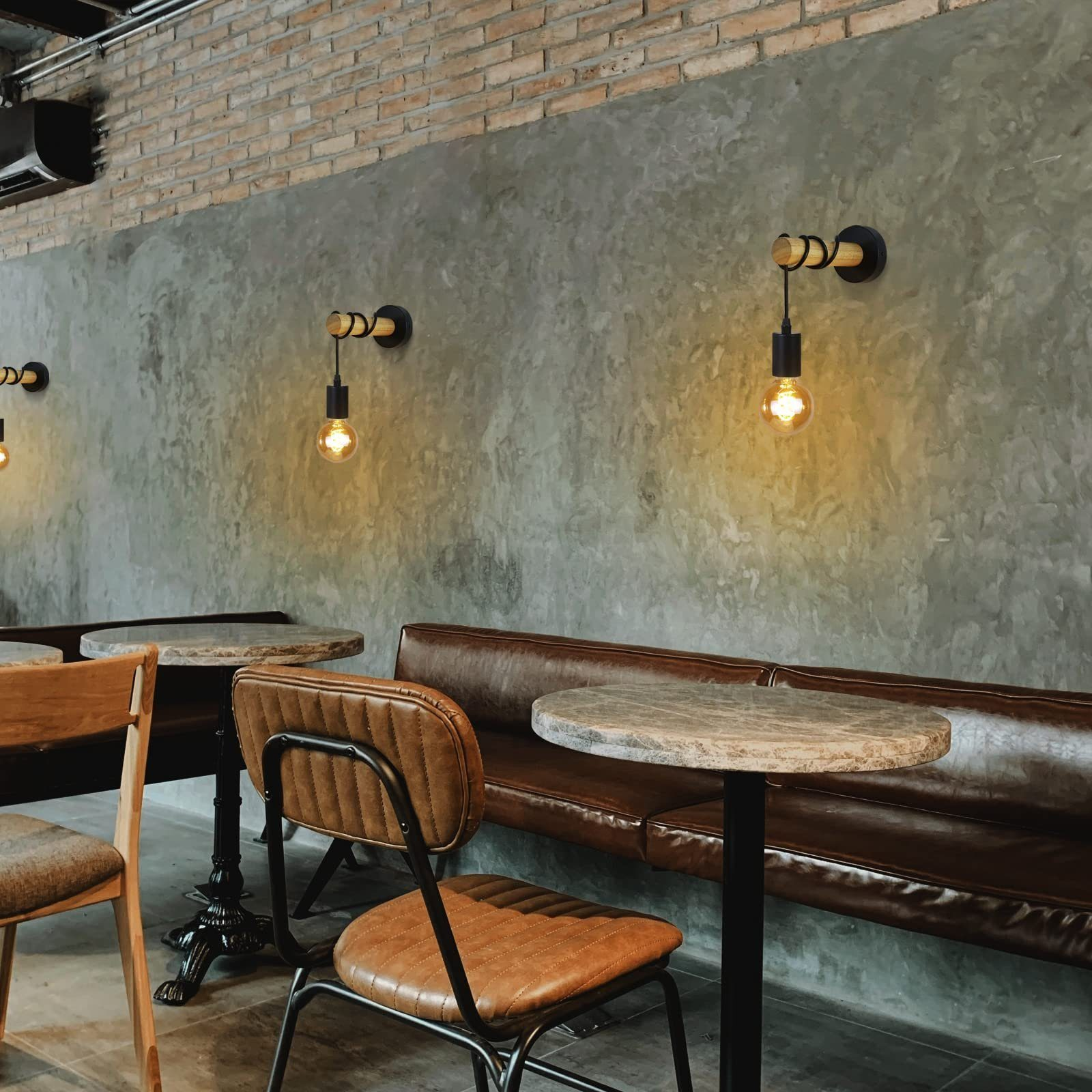 Interno di un caffè con tre lampade da parete, tavoli, sedie e un divano in pelle contro un muro grigio testurizzato.