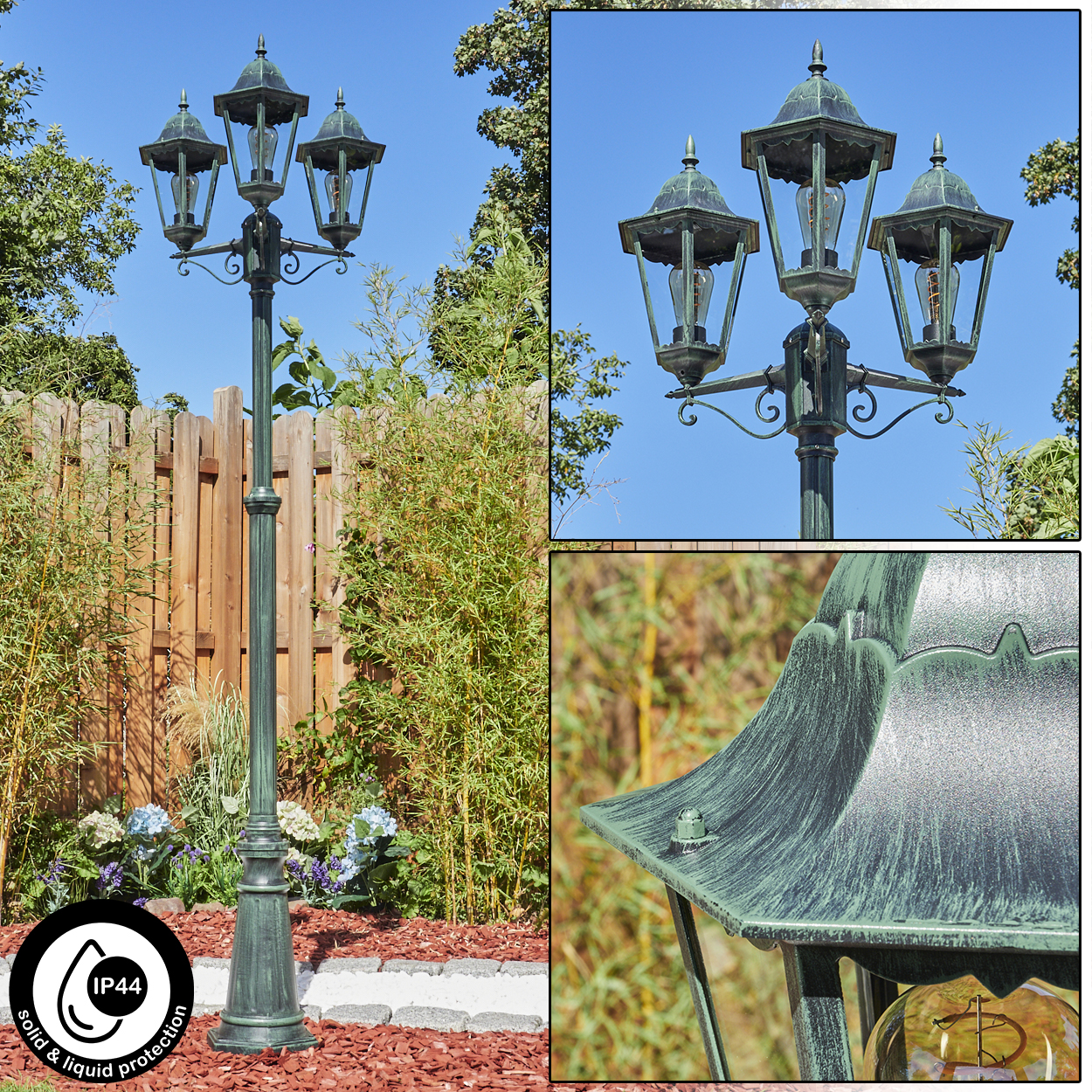 Eine Vintage-Straßenlaterne mit drei Lampen steht in einem Garten mit Bäumen, Pflanzen und einem Holzzaun vor blauem Himmel.