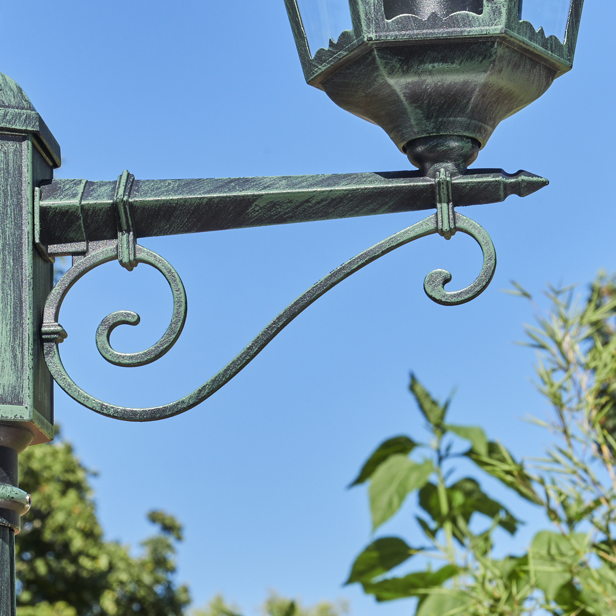 Eine Nahaufnahme zeigt den Arm einer Straßenlaterne im Vintage-Stil mit einem geschwungenen Design vor einem strahlend blauen Himmel.