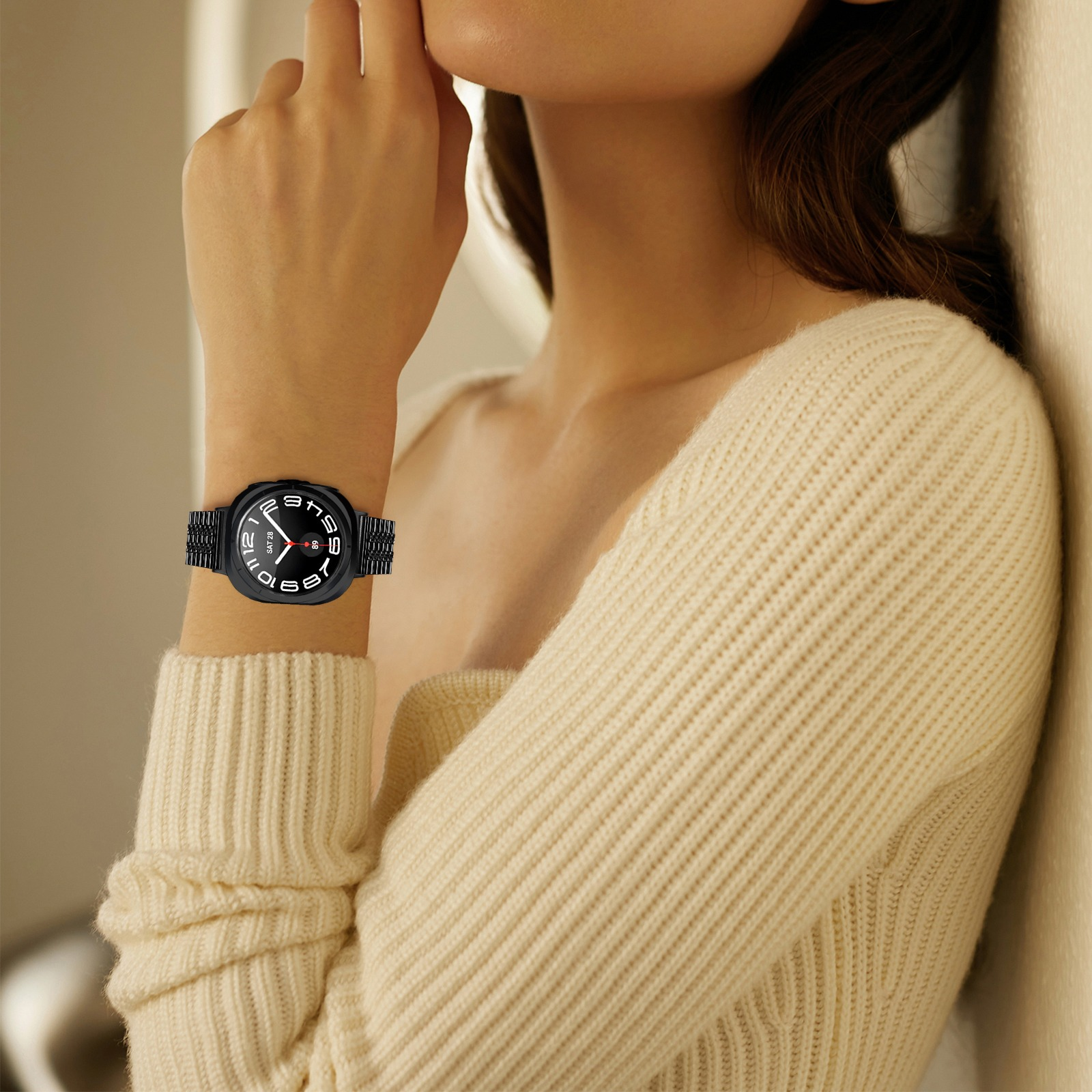 Una donna indossa un orologio nero con quadrante bianco al polso, in posa contro un muro color crema.