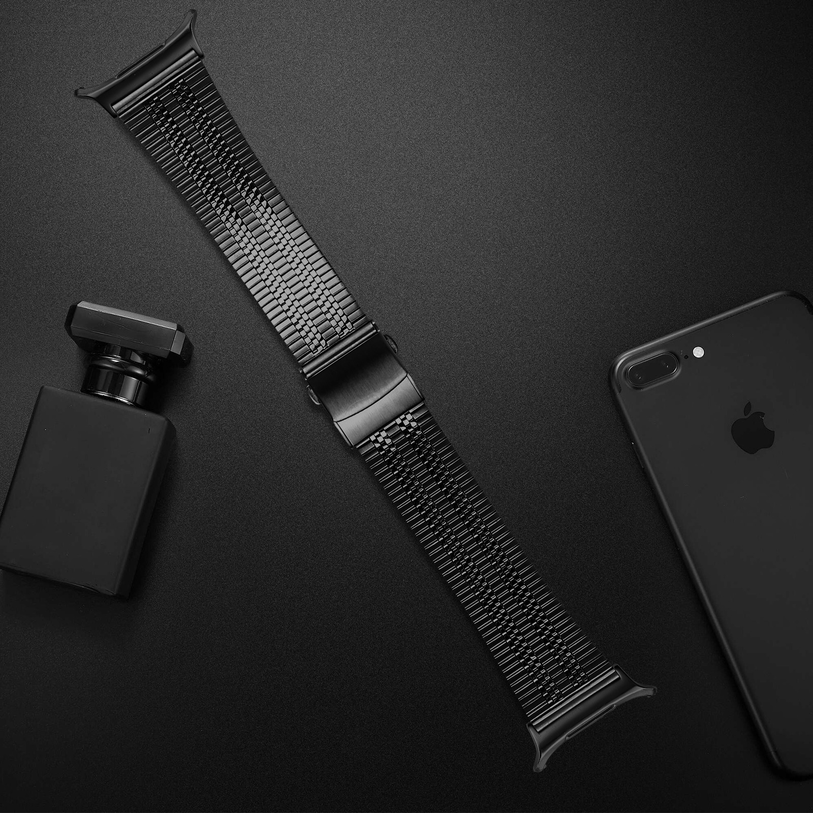 Un cinturino nero per orologio, un flacone di profumo nero e uno smartphone nero sono su una superficie nera.