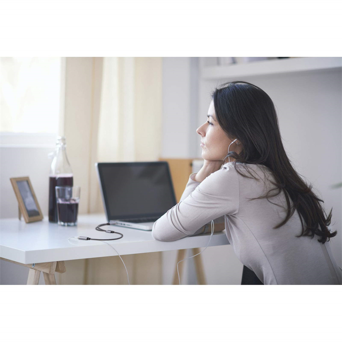 Eine Frau schaut auf einen Laptop mit Kopfhörern. Auf dem Tisch stehen eine Flasche und ein Glas.