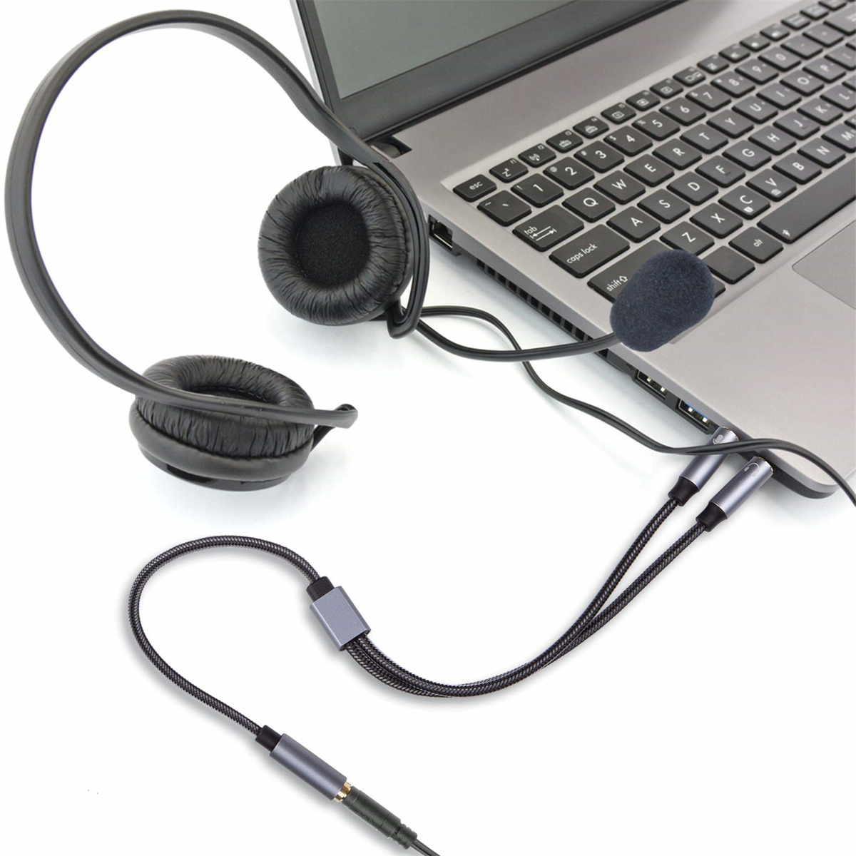 Ein schwarzes Headset mit Mikrofon ist an einen grauen Laptop auf weißem Hintergrund angeschlossen.