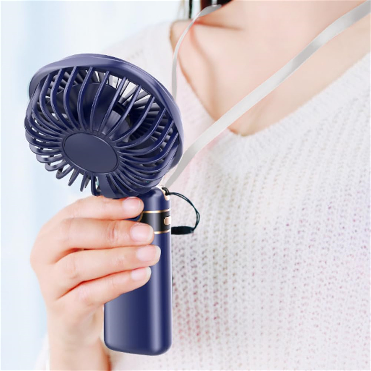 Eine Frau hält einen blauen Handventilator mit einem weißen Schlüsselband um den Hals.