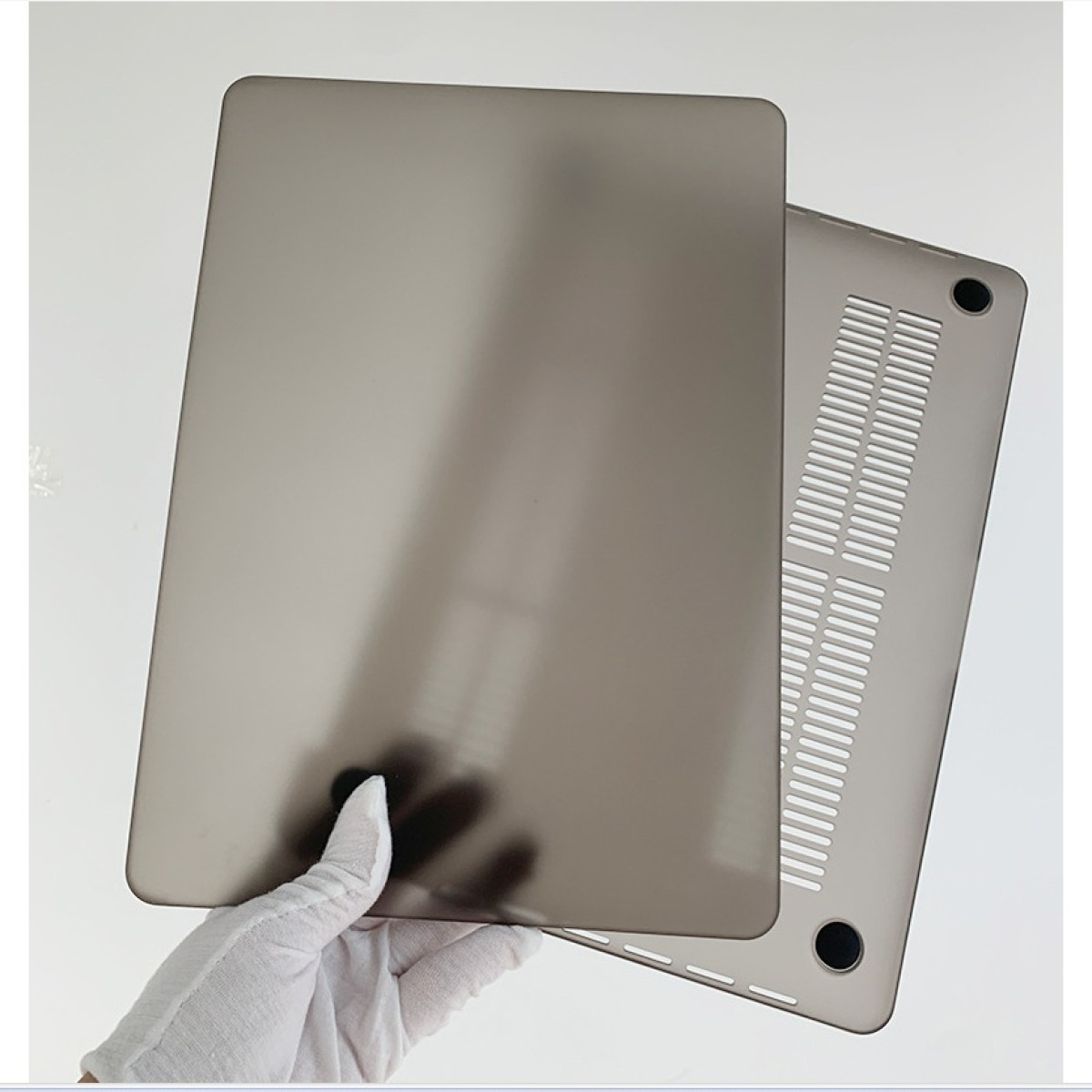 Graue Laptop-Hülle, vom Unterteil getrennt. Eine Hand mit weißem Handschuh hält ein Teil.