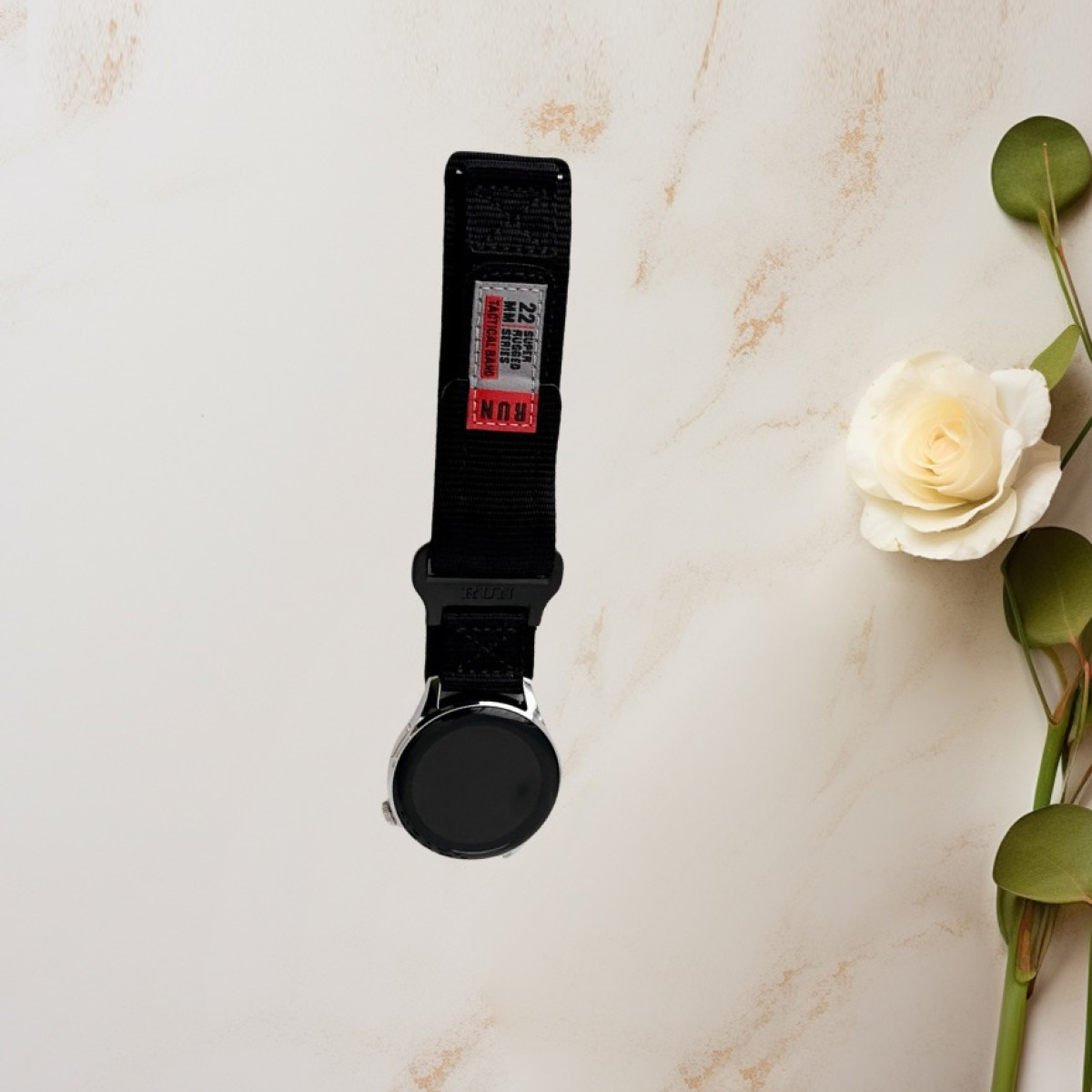 Un orologio con cinturino nero e un fiore bianco sullo sfondo.