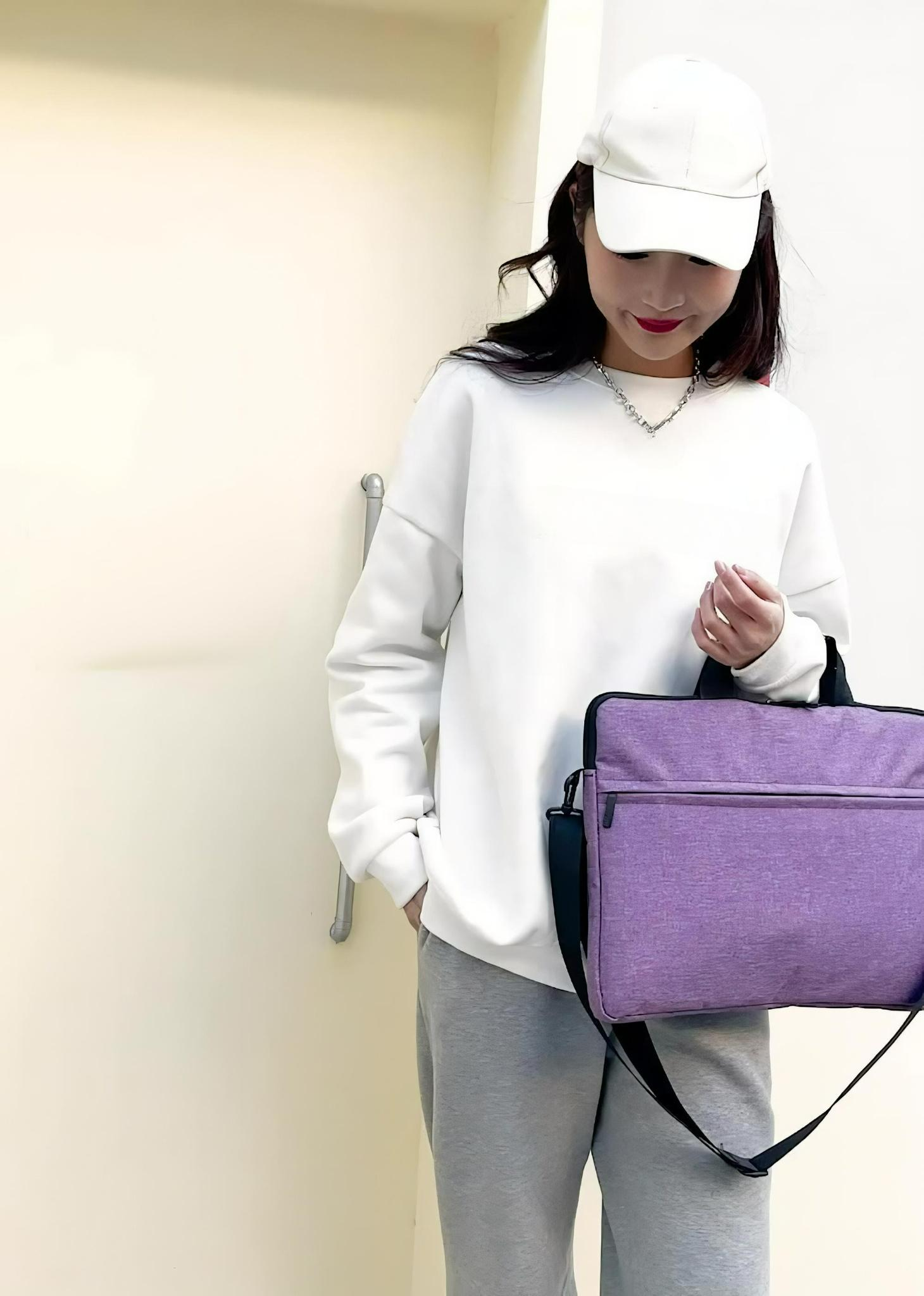 Eine Frau mit weißem Sweatshirt und Mütze, die eine lila Laptoptasche mit schwarzem Schultergurt hält.