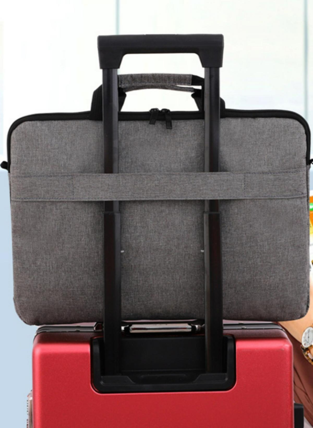 Graue Laptoptasche, die in einem Flughafen an einem roten Koffergriff befestigt ist und Reisekomfort demonstriert.