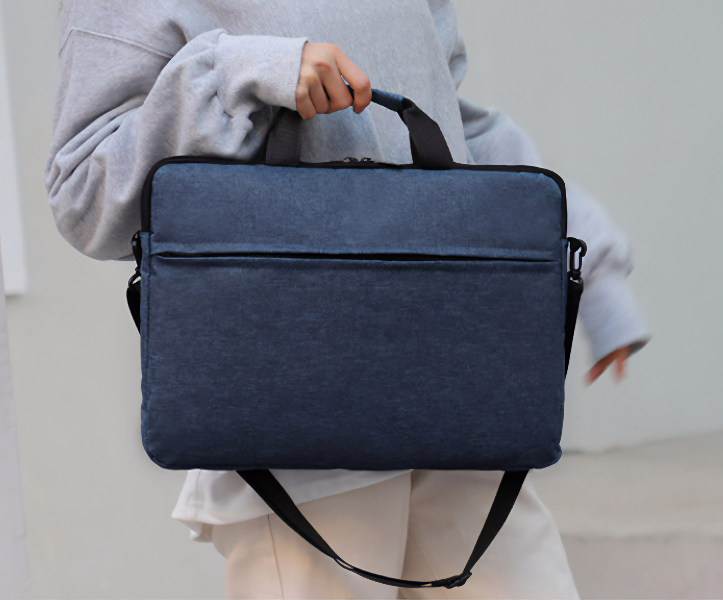 Eine Person hält eine blaue Laptoptasche mit schwarzen Griffen und Riemen.