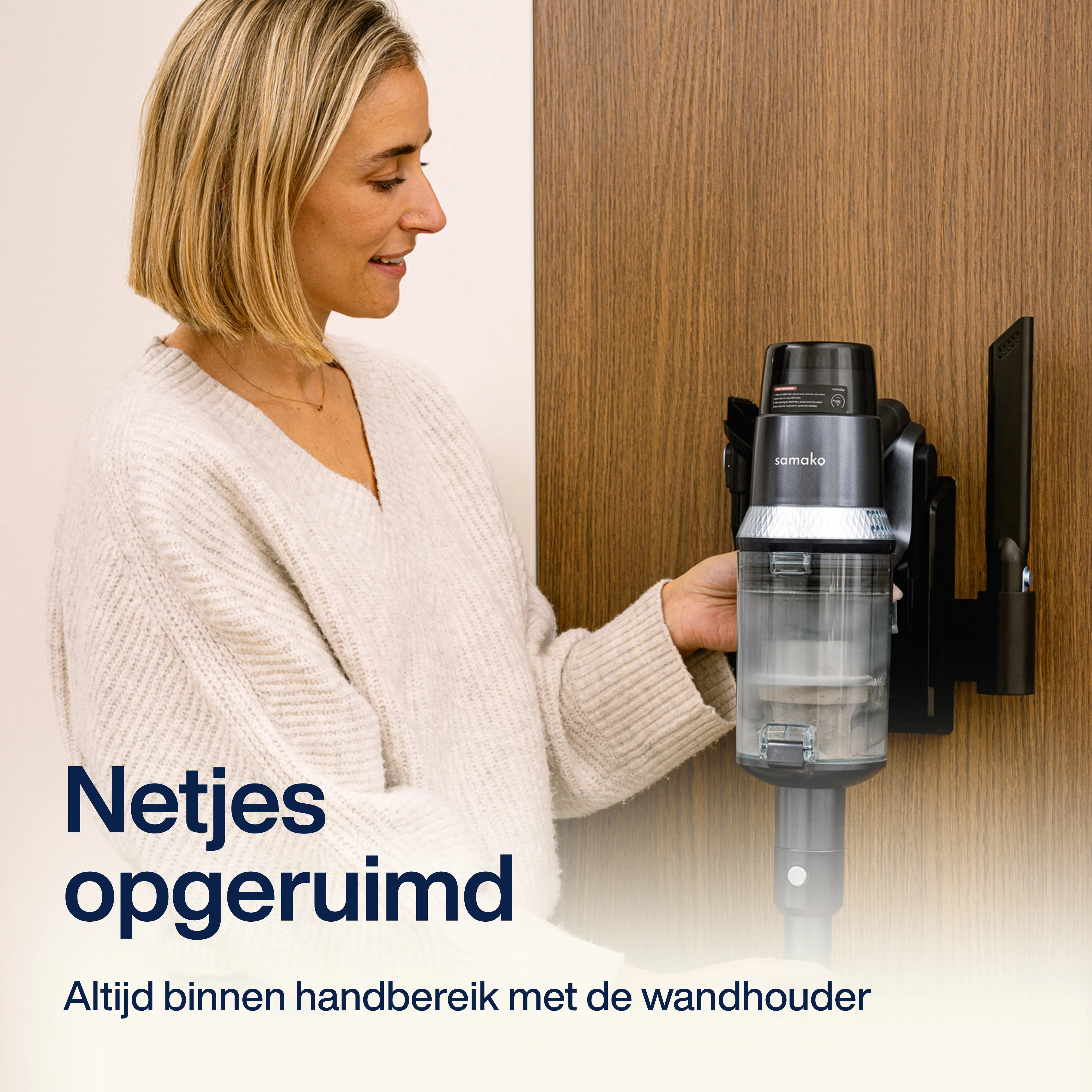 A woman mounts a gray vacuum cleaner on a black wall mount. The vacuum cleaner is being placed for storage.