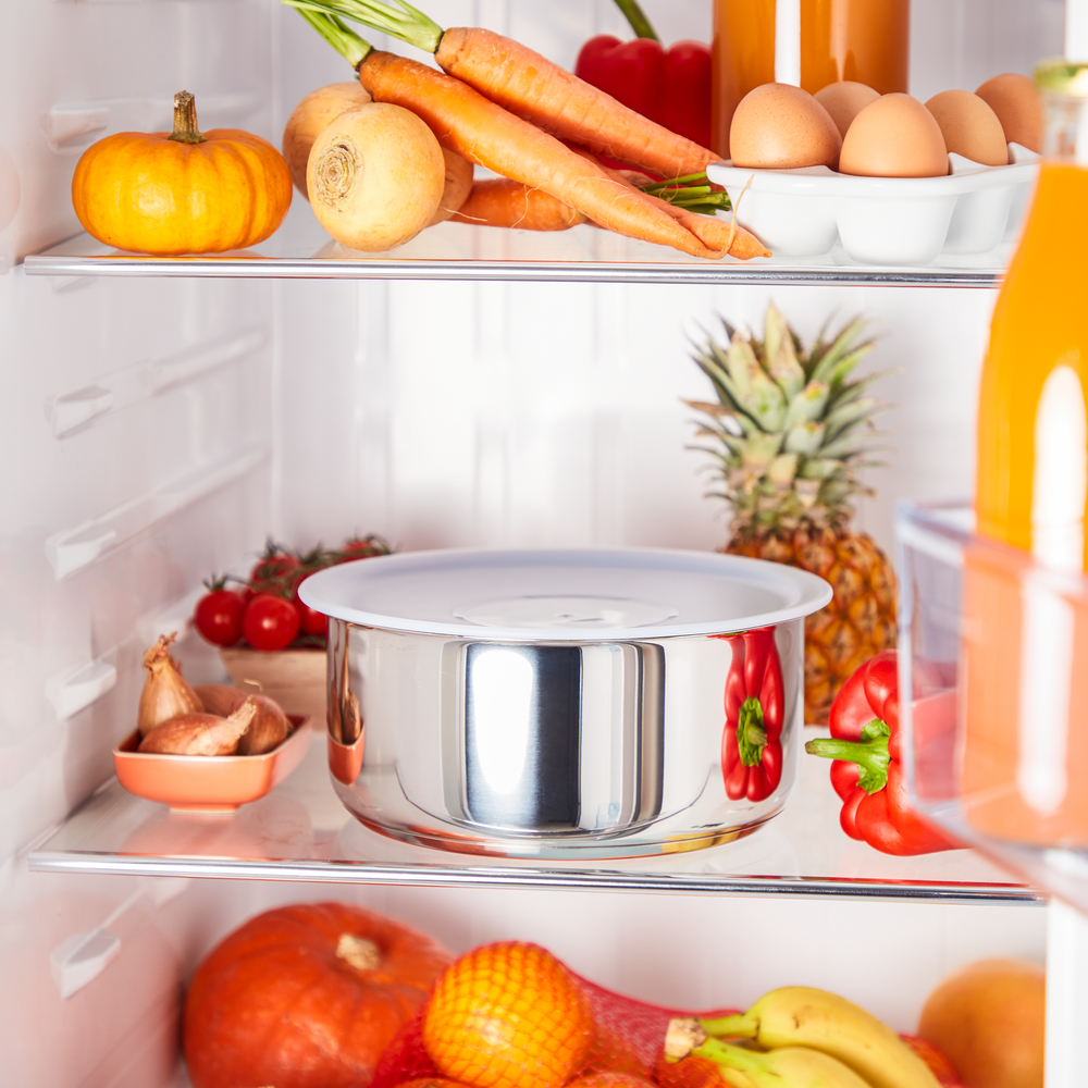 Wewnątrz lodówki ze świeżymi produktami: dynia, marchew, jajka, ananas, pomidory i metalowy pojemnik.