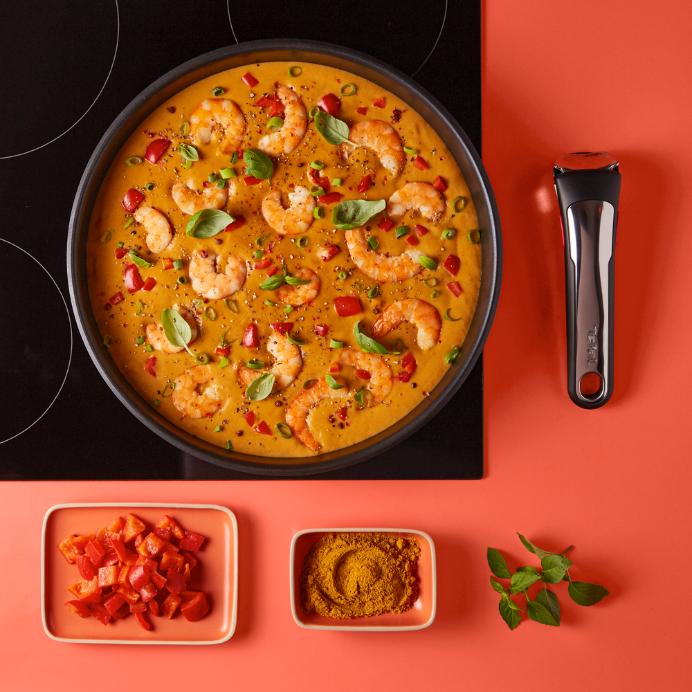 Curry z krewetek w garnku na kuchence, z czerwoną papryką, curry w proszku i bazylią.