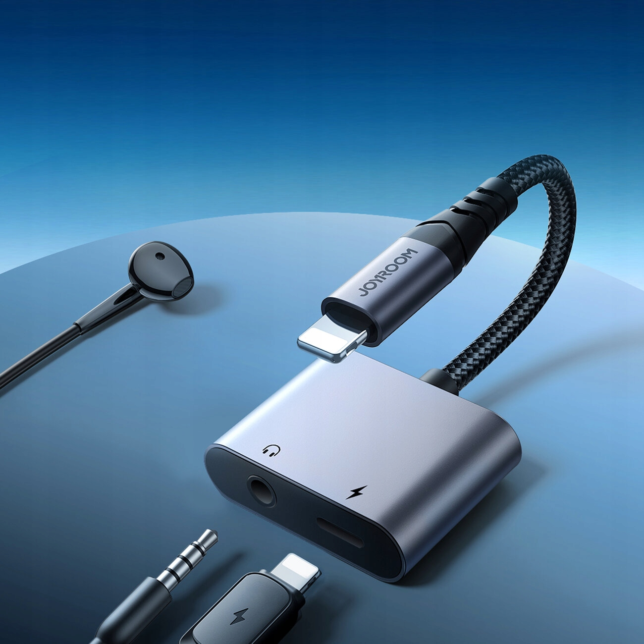 Un adattatore Joyroom con un cavo intrecciato e varie porte è mostrato su uno sfondo blu sfumato con un auricolare.